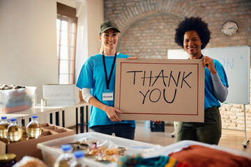 Wall Mural - Happy female volunteers with 'Thank you' placard at donation center looking at camera.