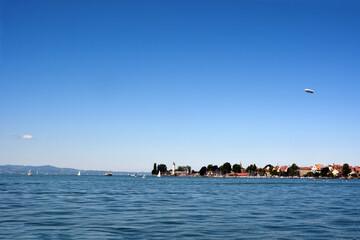 Seascape on the far shore with ancient houses located on the embankment. Yachts float near the shore. An airship is flying in the sky