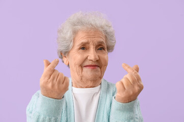 Poster - Senior woman making heart with her fingers on lilac background, closeup