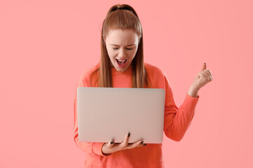 Angry female programmer with laptop on pink background