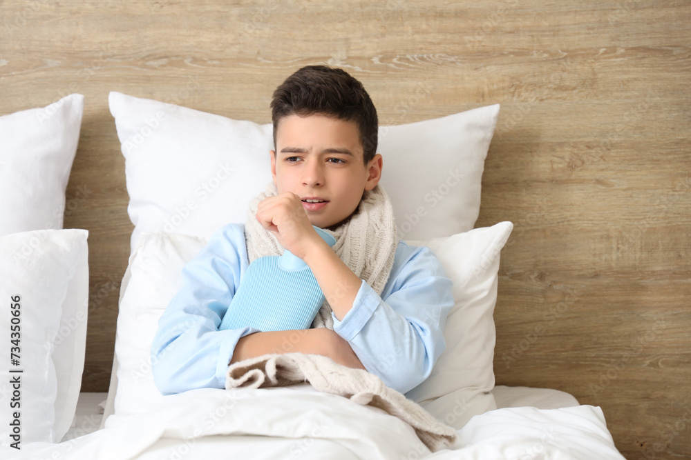 Sick little boy with hot water bottle coughing in bedroom