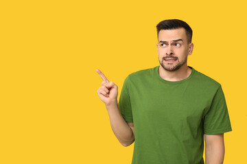 Poster - Handsome ashamed young man pointing at something on yellow background