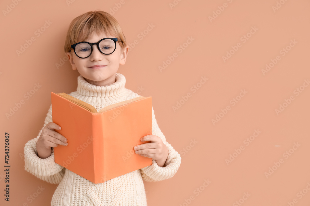 Cute little boy in eyeglasses with open book against color wall