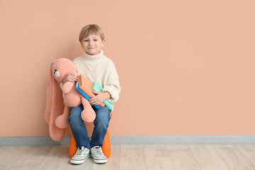 Canvas Print - Cute little boy with toy bunny and books sitting on chair against color wall