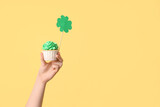 Fototapeta Mapy - Female hand with tasty cupcake and paper clover for St. Patrick's Day on beige background