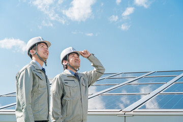 Canvas Print - 太陽光発電・ソーラーパネルの前に立つ電力会社・電気工事業者の作業着姿の技術者（クリーンエネルギー）
