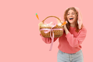 Wall Mural - Beautiful young happy woman in bunny ears with Easter basket on pink background