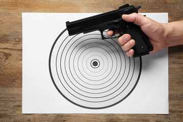 Man with handgun and shooting target on wooden table, top view
