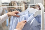 Fototapeta Kuchnia - Dry-cleaning service. Woman taking shirt in plastic bag from rack indoors, closeup