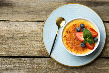 Poster - Delicious creme brulee with berries and mint in bowl on wooden table, top view. Space for text