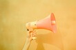 vibrant image capturing a hand holding a coral-colored megaphone against a bright yellow background