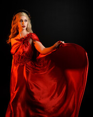 Wall Mural - Close up portrait of beautiful blonde model wearing flowing red silk toga gown and crown, dressed as ancient mythological fantasy goddess. Graceful elegant pose isolated on dark studio background.