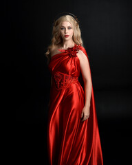 Poster - Close up portrait of beautiful blonde model wearing flowing red silk toga gown and crown, dressed as ancient mythological fantasy goddess. Graceful elegant pose isolated on dark studio background.