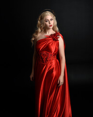 Poster - Close up portrait of beautiful blonde model wearing flowing red silk toga gown and crown, dressed as ancient mythological fantasy goddess. Graceful elegant pose isolated on dark studio background.