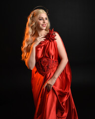 Canvas Print - Close up portrait of beautiful blonde model wearing flowing red silk toga gown and crown, dressed as ancient mythological fantasy goddess. Graceful elegant pose isolated on dark studio background.