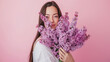 Portrait of a beautiful young woman holding lilac flowers on pink background. copy space