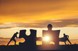 Silhouette of a team folding a puzzle against a sunset background, business and teamwork concept