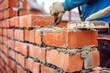 worker stacking red bricks on a new wall, with mortar and trowel