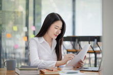 Happy Asian Young Businesswoman Holding Documents Folders In Office Working Space, Asian Female Employee Using Laptop Talking On The Phone At Workplace.