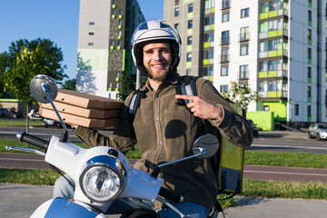 A smiling courier with pizza boxes is sitting on a scooter outside