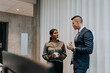 © Maskot - Young businessman discussing with businesswoman standing in office