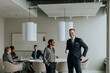 © Maskot - Smiling mature businesswoman standing by young businessman with coffee cup in board room