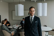 © Maskot - Portrait of confident young businessman standing in board room during meeting