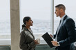 © Maskot - Side view of smiling business colleagues with coffee cup and document standing in office