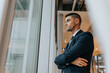 © Maskot - Thoughtful businessman standing with arms crossed looking out through window at office