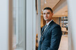 © Maskot - Portrait of confident businessman standing near window at office
