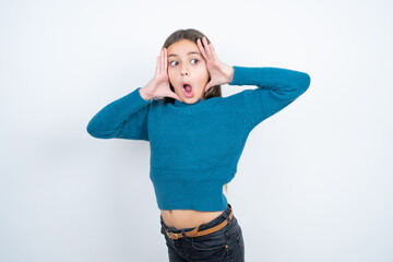 beautiful kid girl wearing blue sweater with scared expression, keeps hands on head, jaw dropped, ha