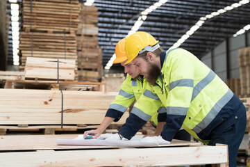 Warehouse and factory concept. Group of male warehouse workers working and discussing structure blueprint building in lumber storage warehouse