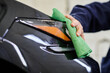 cropped view of dedicated hard working specialist in uniform using rag to clean black modern car