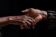 Two African hands clasp together, one younger, one older, against a dark backdrop, portraying strength and unity in family ties.
