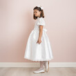 brunette girl 9 years old in a white festive dress on a pale pink background, dress for a wedding, first communion, birthday, celebration