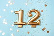 © Anna - Gold candles in the form of number twelve on blue background with confetti. 12 years celebration.