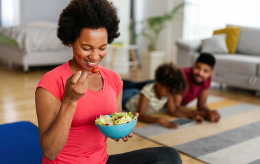 Wall Mural - African american woman with family on background eating a healthy salad after workout. Fitness