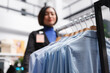 Formal shirts hanging on display rack while asian woman assistant working in clothing store selective focus. Menswear garment on hangers in shopping mall boutique closeup