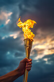 Fototapeta  - Hand holding a golden Olympic torch with a bright flame against a dramatic cloud-filled sky, symbolizing the Olympic Games in Paris, with copy space for text