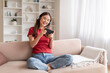 © Prostock-studio - Cheerful korean woman playing video games on smartphone while relaxing on couch