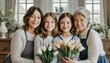 Kobiety i dziewczynki z rodziny wielopokoleniowej siedzące obok siebie i trzymające w dłoniach kwiaty. Międzynarodowy Dzień Kobiet