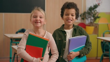 Wall Mural - Happy laughing satisfied funny African and Caucasian little school children multiracial diverse girl and boy kids pupils schoolchildren together class study primary education laugh smile hold books