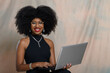 © Edson Souza - woman holding laptop, typing on keyboard and looking at camera, black woman
