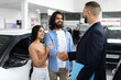 © Prostock-studio - Happy young eastern couple buying new car at dealership salon