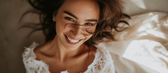 Wall Mural - Beautiful young woman with a radiant smile lying comfortably on a cozy bed at home