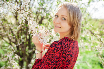 Wall Mural - Charming cute woman posing in flowers in a blooming garden park on a sunny spring day. The concept of unity with nature.