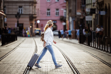 Wall Mural - Woman tourist with suitcase walks across city street. Secure  journey with reliable travel insurance