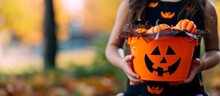 Adorable Little Girl Happily Holding A Pumpkin-shaped Halloween Bucket During Trick Or Treating