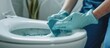 Person wearing a blue glove cleaning a toilet bowl with disinfectant and sponge at home