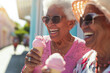Couple of cheerful elderly female friends eating ice cream outdoors on sunny summer day. Senior ladies sharing a dessert in outdoor cafe.